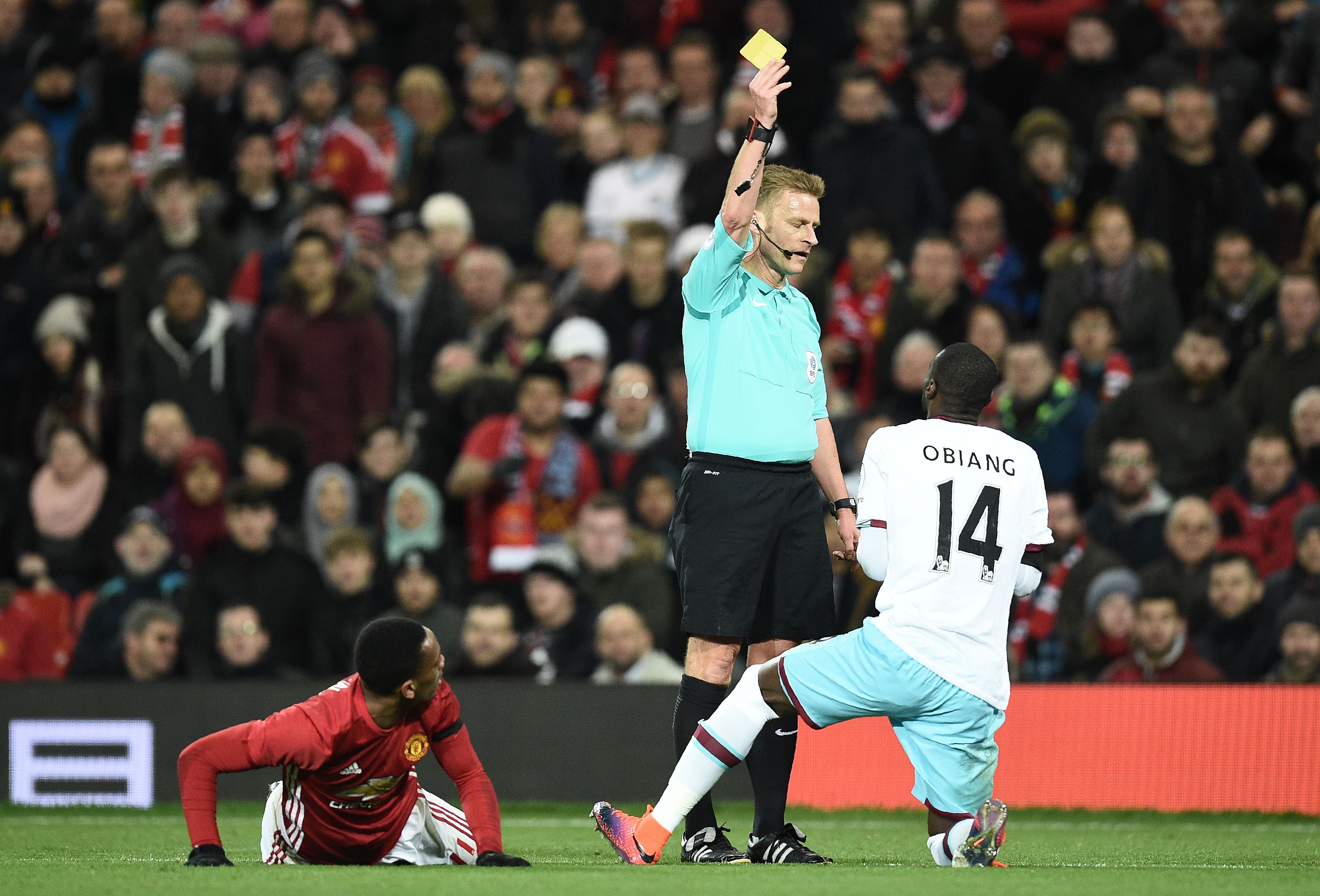 Referee Mike Jones (C) shows a yellow card to West Ham United's Spanish midfielder Pedro Obiang (R) for his challenge on Manchester United's French striker Anthony Martial during the EFL (English Football League) Cup quarter-final football match between Manchester United and West Ham United at Old Trafford in Manchester, north west England, on November 30, 2016. / AFP / Oli SCARFF / RESTRICTED TO EDITORIAL USE. No use with unauthorized audio, video, data, fixture lists, club/league logos or 'live' services. Online in-match use limited to 75 images, no video emulation. No use in betting, games or single club/league/player publications.  /         (Photo credit should read OLI SCARFF/AFP/Getty Images)