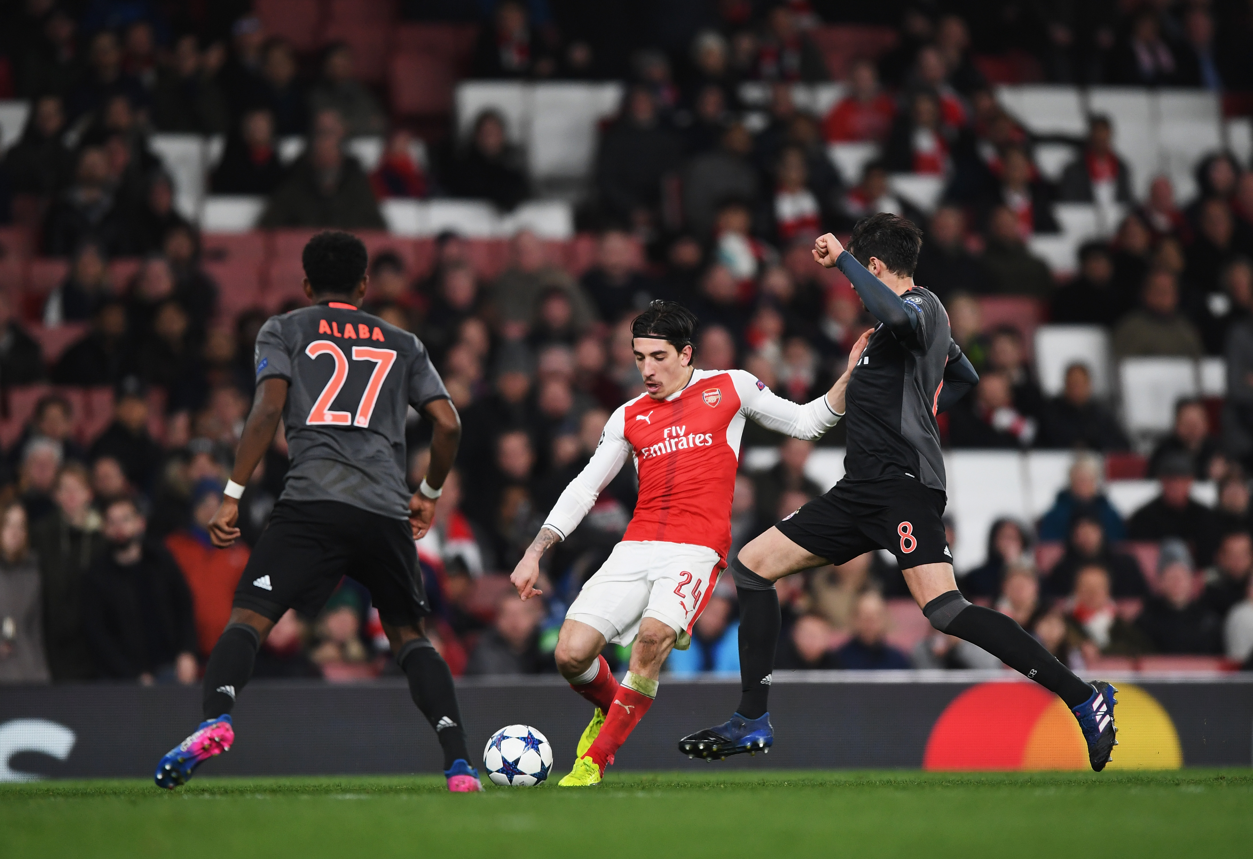 LONDON, ENGLAND - MARCH 07:  Hector Bellerin of Arsenal takes on David Alaba and Javi Martinez of Bayern Muenchen with a back drop sparsely populated seats during the UEFA Champions League Round of 16 second leg match between Arsenal FC and FC Bayern Muenchen at Emirates Stadium on March 7, 2017 in London, United Kingdom.  (Photo by Shaun Botterill/Getty Images)