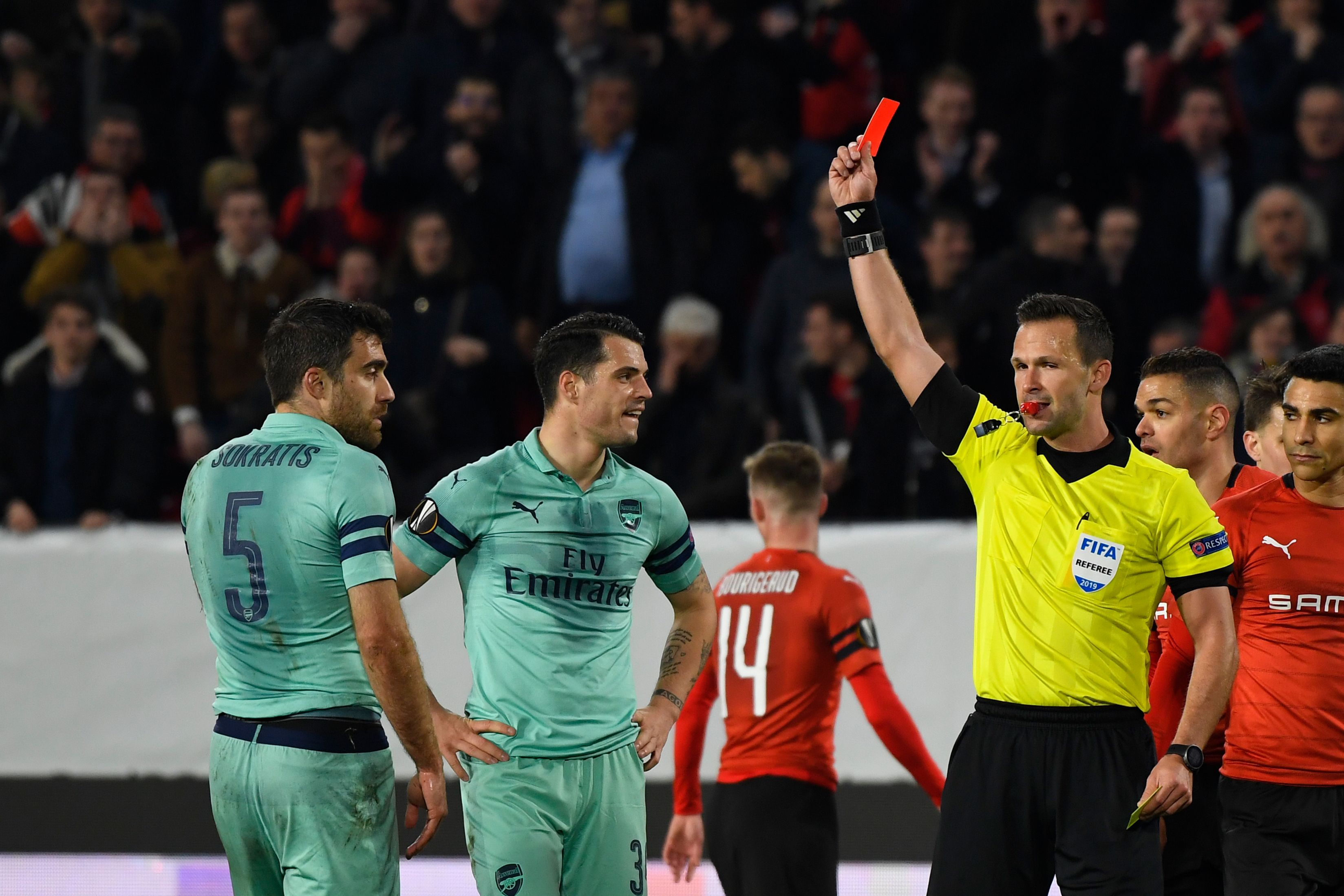 Slovak referee Ivan Kruzliak (R) shows a red card to Arsenal's Greek defender Sokratis Papastathopoulos (L) during the UEFA Europa League round of 16 first leg football match between Stade Rennais FC and Arsenal FC at the Roazhon Park stadium in Rennes, northwestern France on March 7, 2019. (Photo by DAMIEN MEYER / AFP)        (Photo credit should read DAMIEN MEYER/AFP/Getty Images)