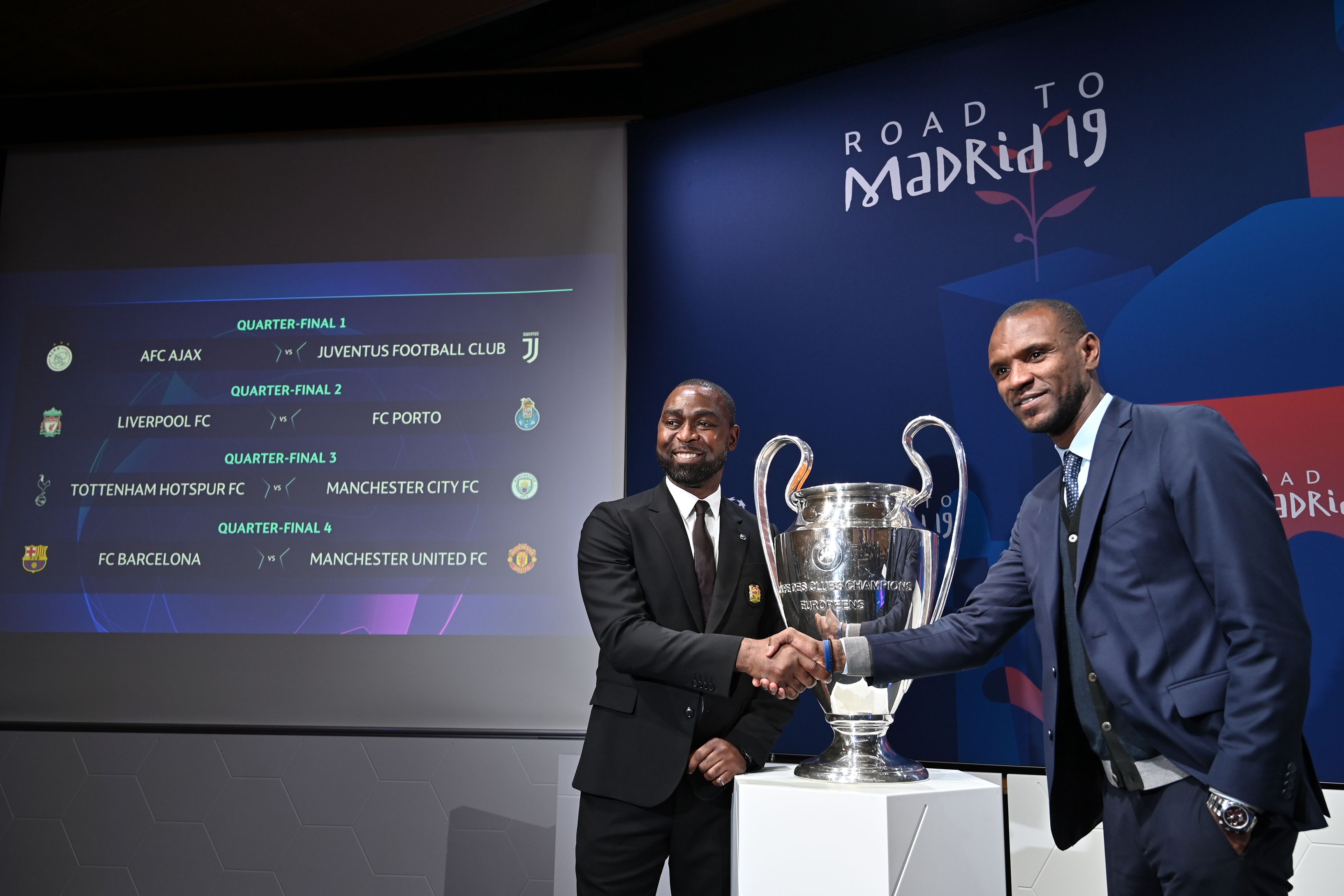Manchester United football club ambassador Andy Cole (RL shakes hands with FC Barcelona ambassador Eric Abidal next to results of the draw for the Champions league quarter-final and the competition's trophy, on March 15, 2019 in Nyon. (Photo by Fabrice COFFRINI / AFP)        (Photo credit should read FABRICE COFFRINI/AFP/Getty Images)